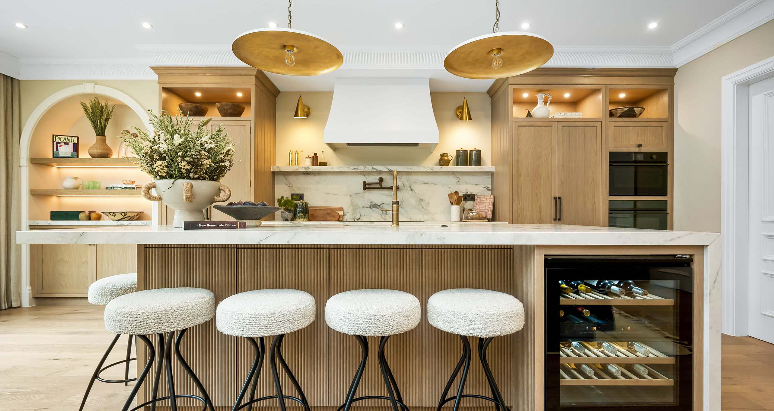Luxury Bespoke Lyon Framed Kitchen Luxury bespoke Lyon Framed kitchen handcrafted in Nottinghamshire by Charles Yorke, featuring a fluted wooden island with marble countertops, backless bouclé bar stools, and an integrated wine cooler.